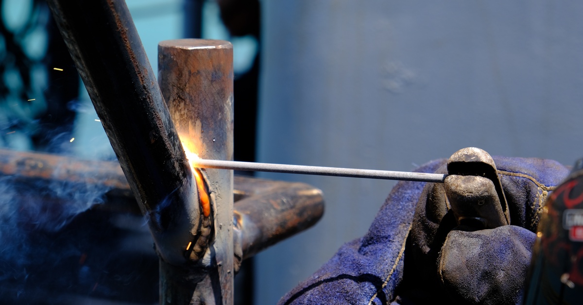 A close-up, highly detailed shot of a welder using stick welding to merge two small, thin metal joints together.