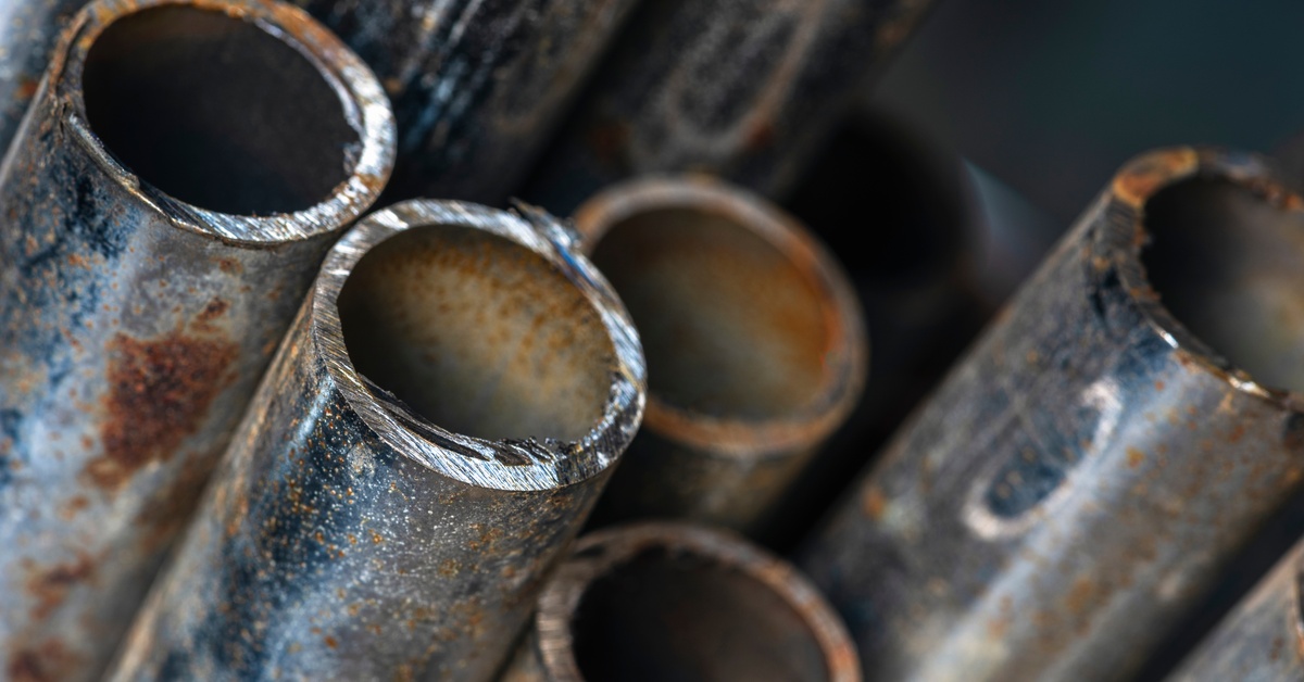 A detailed close-up shot of a collection of metal pipes clustered together, with rust forming on the interiors and exteriors.