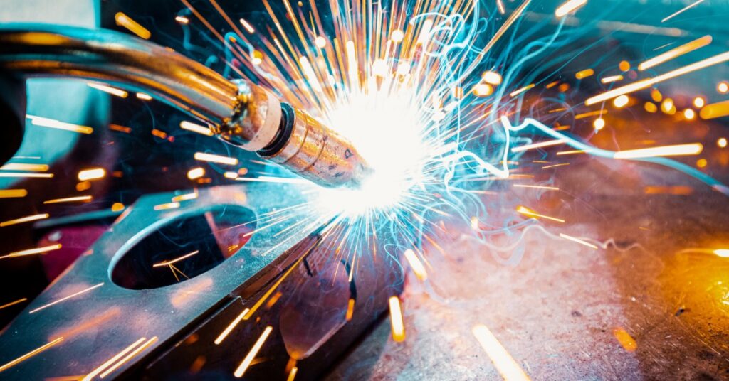 A close view of bright welding sparks flying from metal with blurred light trails against a dark background.