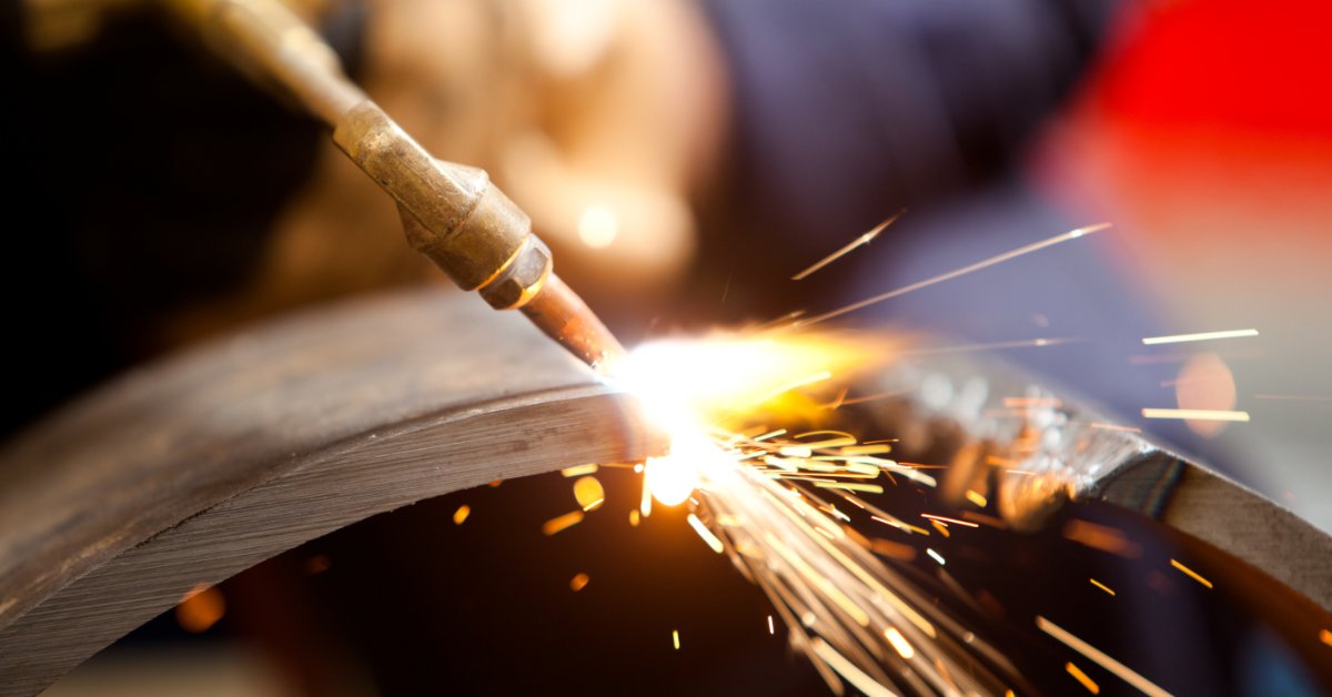 A close-up view of an acetylene torch cutting metal, with bright sparks and an orange glow around the cut.